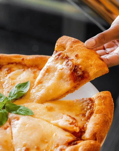 Person picking up a slice of pizza with cheese and basil leaves on a blurred background
