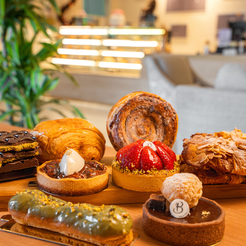 Assorted pastries on a wooden board with a blurred indoor background by Bake N More bakery and pastry manufacturer in Dubai