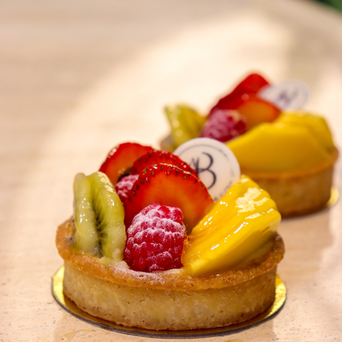 Small fruit tart with strawberries, kiwi, and pineapple on a wooden surface by Bake N More pastry manufacturer in Dubai